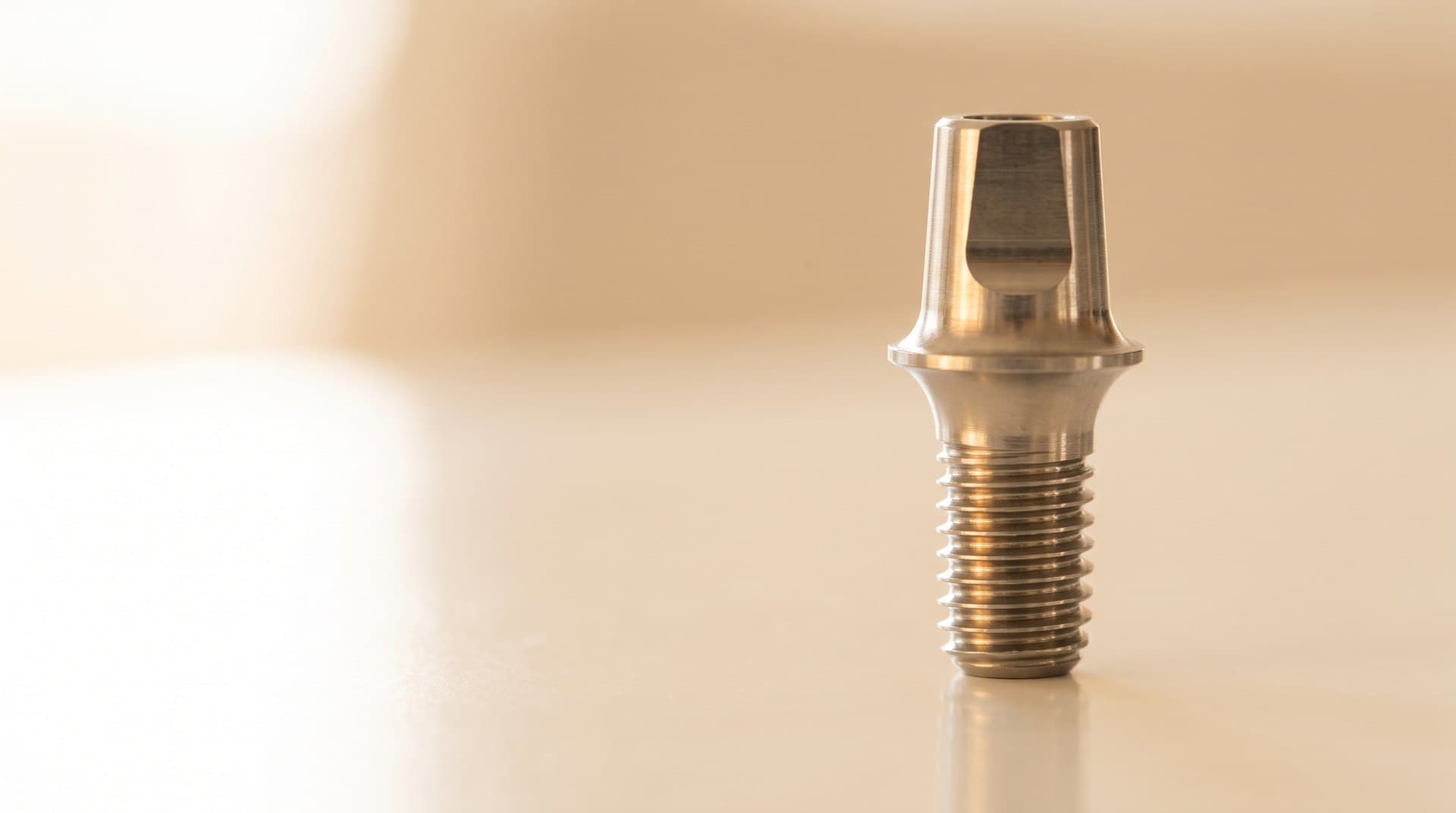 A warm close-up photograph of a titanium dental implant abutment, a small metallic connector post