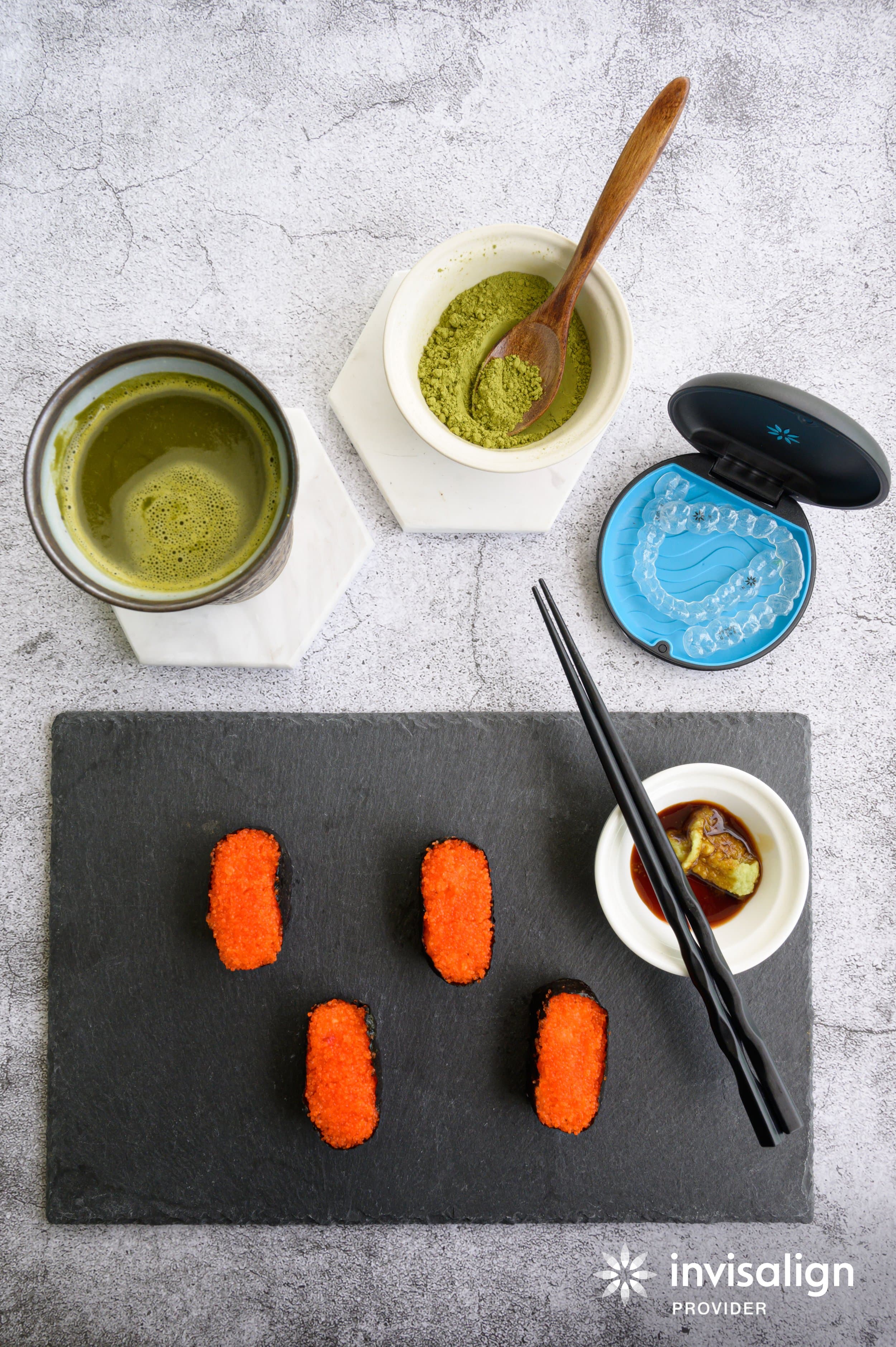 A flat lay of nigiri sushi, matcha tea, chopsticks and an open Invisalign case holding a clear aligner, a reminder to take retainers out before eating, at Align Dental Surgery