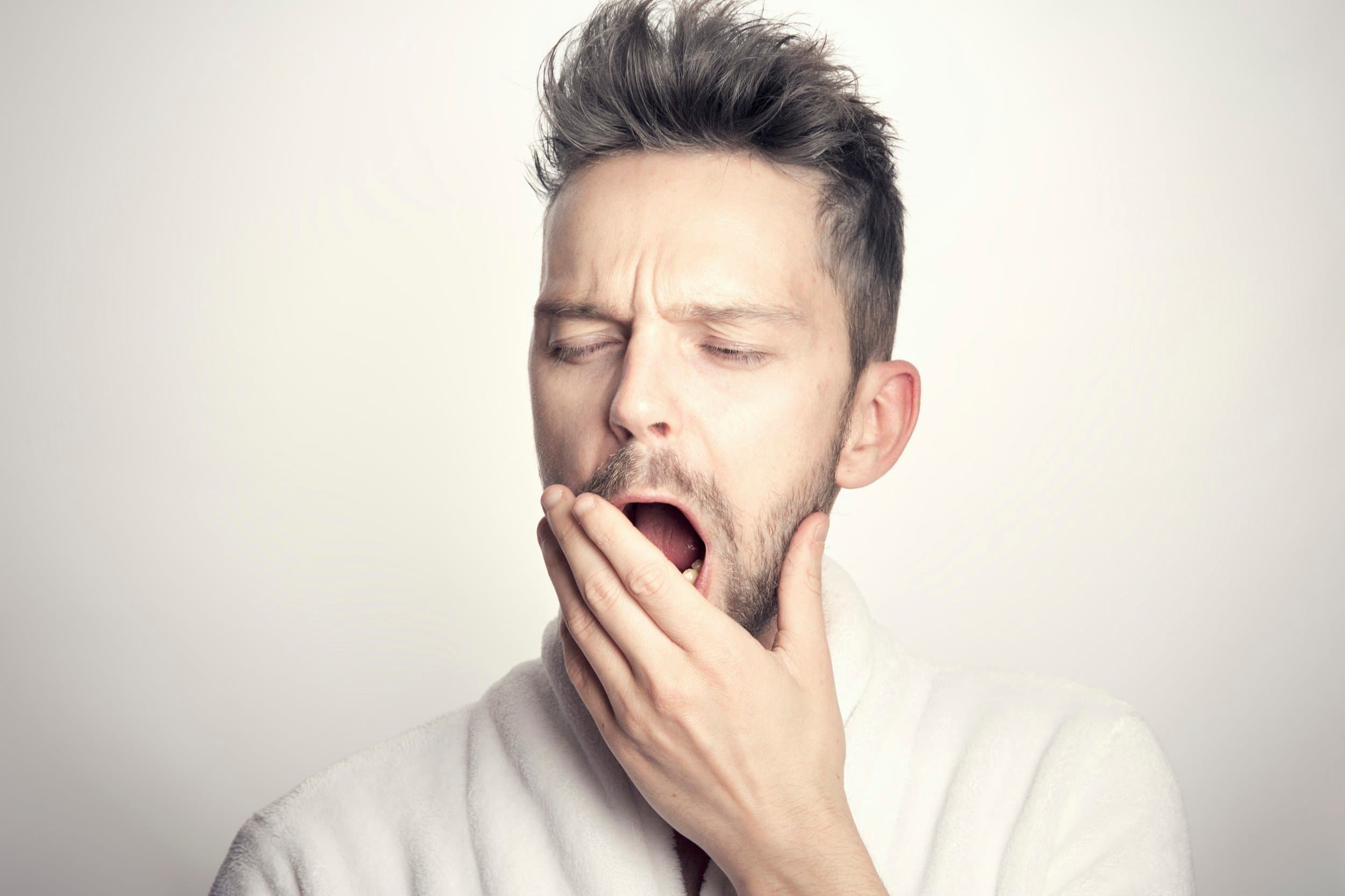 A tired man in a bathrobe yawning, reflecting the daytime fatigue that can signal sleep-related breathing disorders, at Align Dental Surgery