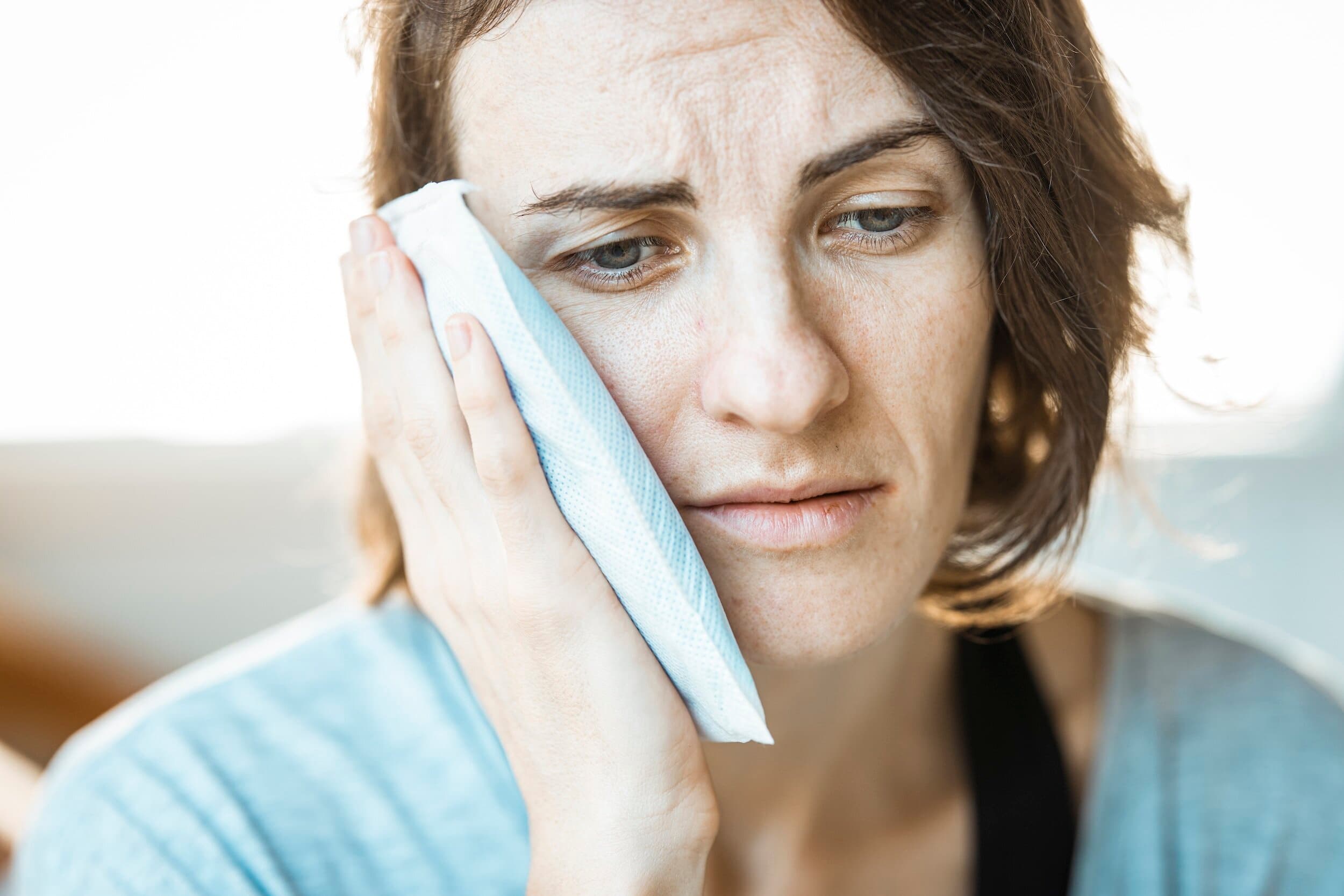 A woman holding a cold compress against her cheek to ease tooth pain